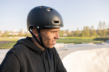 A cyclist stands on a ramp in a park on a spring afternoon with a helmet on his head and looks forward at the ramp wondering if he can pull off a new trick