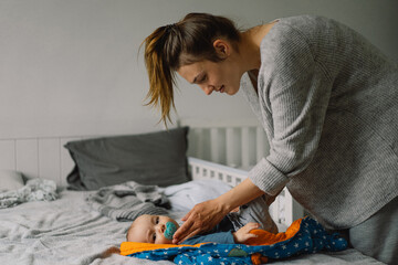 Mom dresses cute little baby boy in a jumpsuit.