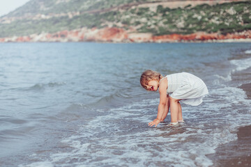 Little adorable girl plays on sea coast. Summer time, vacation concept