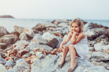 Fototapeta na wymiar Little adorable girl plays on sea coast. Summer time, vacation concept