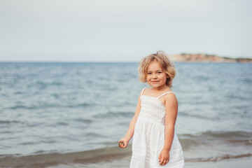 Fototapeta na wymiar Little adorable girl plays on sea coast. Summer time, vacation concept