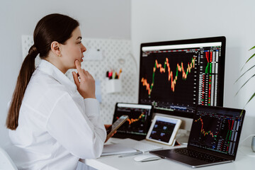 Young female cryptocurrency trader sitting at desk looking at multiple screens monitoring stock financial market. Business woman investor analyst analyze currency growth graph.