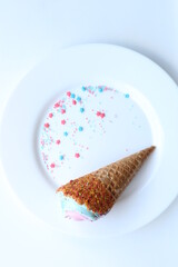 Ice cream cone with pink and blue sugar sprinkles on a white plate