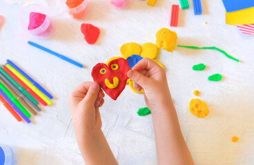 Child playing with plasticine, colorful modeling clay and sculpting heart . Home Education game with clay. Early development . Handmade concept for birthday, mothers day or valentines day - obrazy, fototapety, plakaty