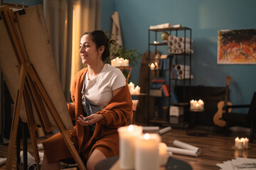 A young, disheveled artist sits in the living room with all her drawings lying on the floor, on a cabinet. The woman is happy and admires her new drawing