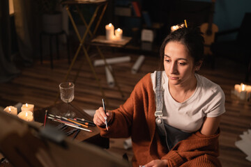 Female sits at work on a new drawing and contemplates sketching a portrait with the pencil of her choice. In the background lie scattered earlier drafts.