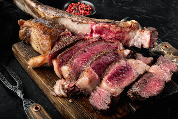 Grilled steak on the bone sliced, medium rare tomahawk cut, on wooden serving board, on black stone background