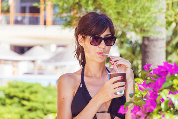 Young Woman with Swimsuit Drinking Cocktail  on a Pool Background. Summer Holiday Concept 