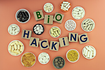 photo on biohacking theme. wooden cubes with the inscription "biohacking", and biologically active supplements, on coral background