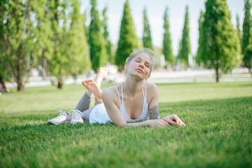 Attractive sportive girl lies on the grass and relaxes in park