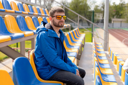 A man with glasses and a jacket at the stadium.