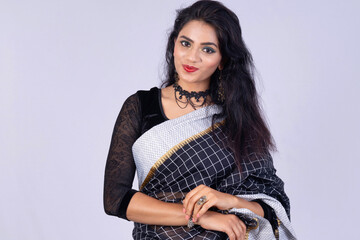 Young Indian woman wearing an elegant black saree. Looking at camera. Smiling. Happy. Grey...