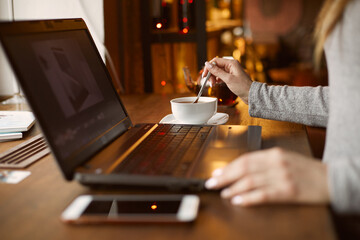 Girl ordering tea in a cafe. Works for a laptop. The mobile phone is on the table. Remote work and freelance work concept.