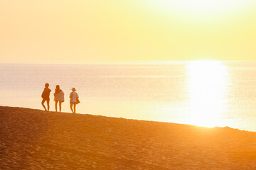 group of friends walking by sandy beach on sunset