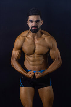 Muscular bodybuilder male in gym. Black background. Front profile. Looking at camera. Showing chest and shoulder muscles