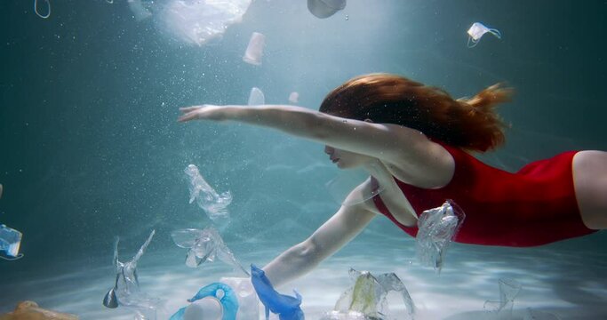 Plastic waste in the ocean. Young female tourist swims through single use packaging garbage under water slow motion.
