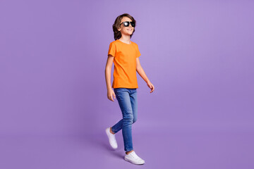 Fototapeta na wymiar Full length body size photo walking small boy wearing casual clothes sunglass smiling isolated pastel purple color background