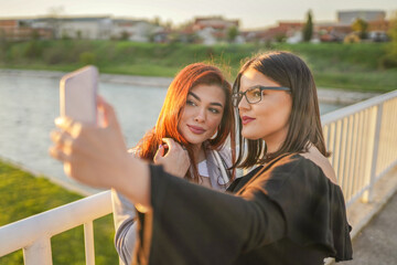 Two female friends standing on bridge and making selfie