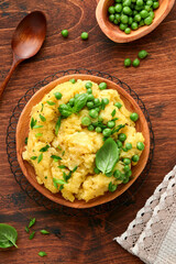 Mashed potato with butter, green peas, onions, basil on a rustic wooden background. Top view with close up.