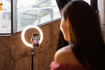 Young woman making photo or video content for social media with smartphone and light of ring lamp....