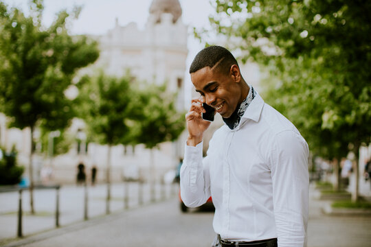 Young African American businessman using a mobile phone while waitng for a taxi on a street