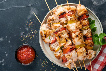 Chicken shish kebab or skewers kebab on wooden board, spices, herbs and vegetables on dark grey...