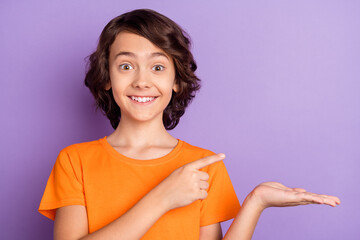 Portrait of attractive cheerful amazed boy holding on palm demonstrating copy space isolated over violet purple color background © deagreez