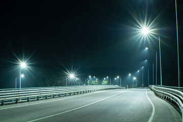 An empty country road with metal bumpers on the edges in the light of streetlights