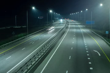 Tuinposter High-speed suburban highway in the light of streetlights. There is a white marking arrow on the asphalt © VeNN