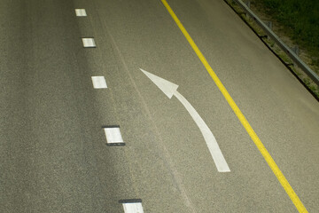 A white direction arrow is drawn on the asphalt, between a broken line and a solid yellow one