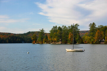 Fototapeta na wymiar Sailboat on calm lake with fall foliage and quaint cabins