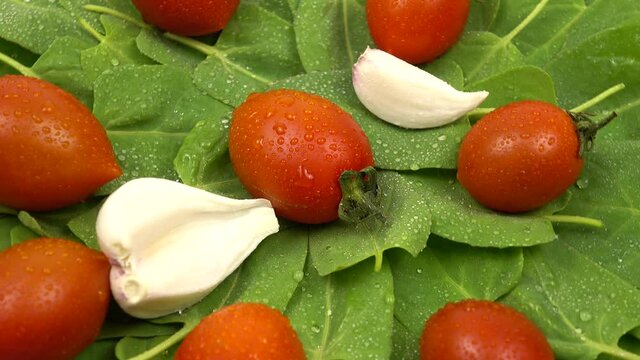 Water droplets lie on the fresh vegetables. Cherry tomatoes, spinach, garlic are on a white table, salad ingredients