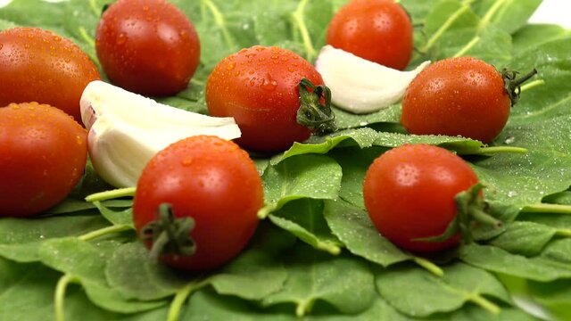 Water droplets lie on the fresh vegetables. Cherry tomatoes, spinach, garlic are on a white table, salad ingredients