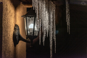 icicles hanging from the roof by a lighted lamp