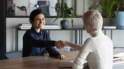 Smiling multiethnic businesswomen shake hands close deal or agreement at meeting in office. Happy...