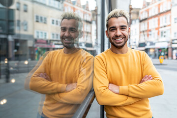 Happy man portrait in London - smiling young man leaning against glass shop window - lifestyle and happiness