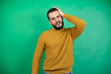 Handsome man wearing casual clothes over isolated green background putting one hand on her head...