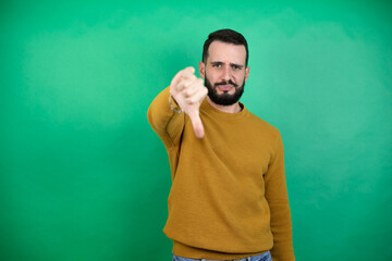 Handsome man wearing casual clothes over isolated green background with angry face, negative sign...