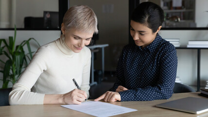 Happy young Caucasian woman sign paper document close deal with Indian business partner or client...