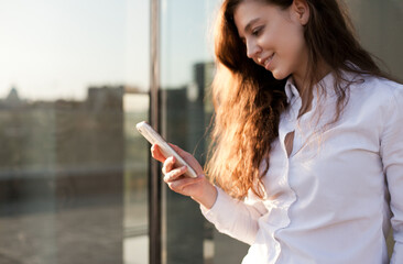Fototapeta premium Young woman holding a mobile phone and smiling, texting or using social media