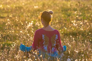 A woman is meditating at sunset in a field