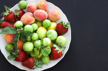 Top view of Fresh summer fruits, plum, peach, apricot, strawberry in plate on black background, copy space, food concept.