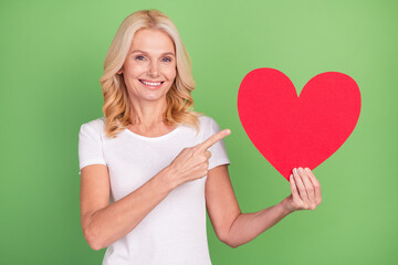 Photo of romantic blond aged lady point heart wear white t-shirt isolated on pastel green color background