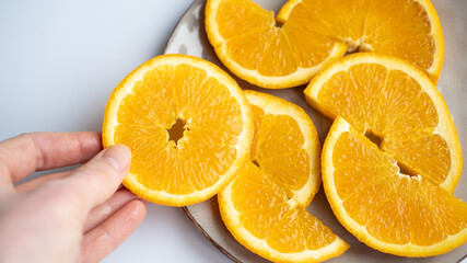 Hand taking a slice of orange from the plate on the table. Orange slice at the hand. Juicy orange on a gray plate