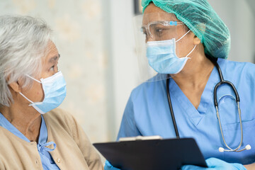 Asian doctor wearing face shield and PPE suit new normal to check patient protect safety infection Covid-19 Coronavirus outbreak at quarantine nursing hospital ward.