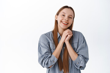 Cute and romantic girl, hands together, smiling and look admiration and love at camera, being...