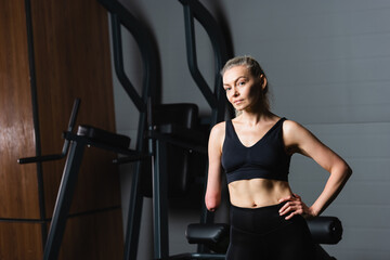 Fototapeta na wymiar amputee woman in black sportswear standing with hand on hip in gym