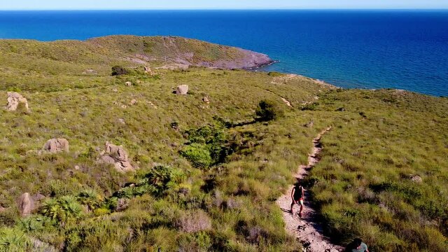 Calblanque coast aerial drone shot of hiking sportsmen walking in mountain against mediterranean seascape. 