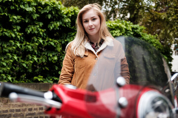 Young blonde woman posing behind of a red scooter.