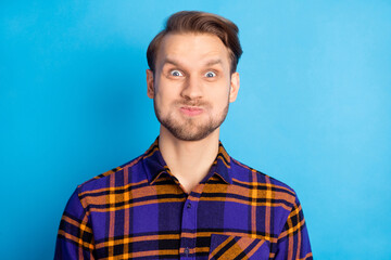 Portrait of attractive cheerful funny man grimacing wearing checked shirt blowing air isolated over bright blue color background